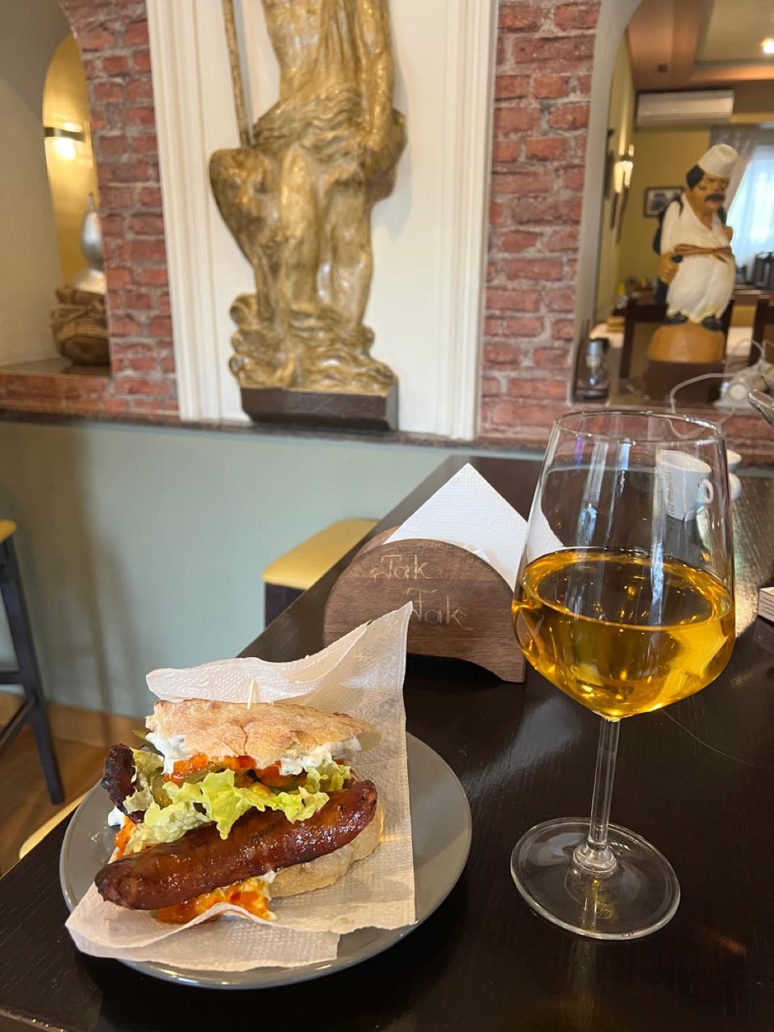 The dining room at Tak Fak — exposed brick, a glass of wine and a grilled sausage sandwich
